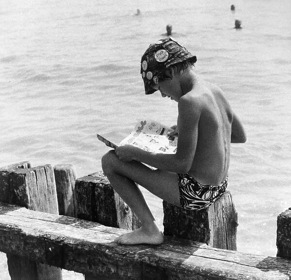 Boy sitting on breakwater reading a comic