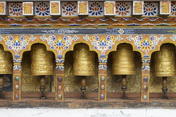 Bhutan. Spinning prayer wheels along a temple wall