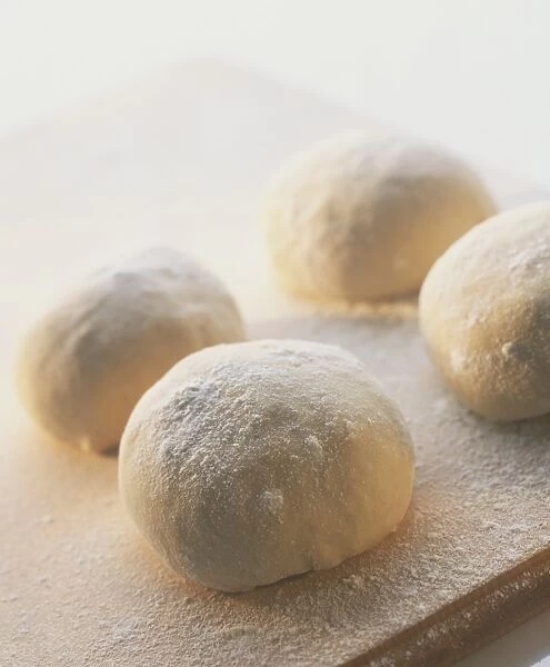 Fresh pizza dough rolled into four round balls, covered in white flour