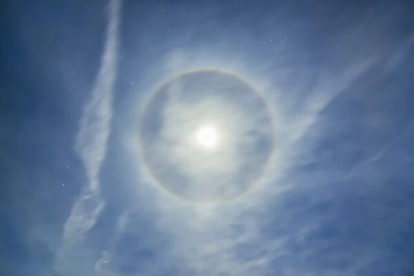 Halo around full moon in a sky of cirrus clouds and contrails
