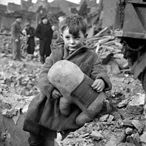 WWII: LONDON, 1945. A boy holding a stuffed animal amid ruins following a German
