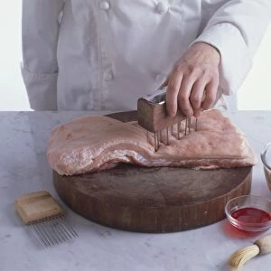Chef using meat tenderiser on pork belly on wooden chopping board, close-up
