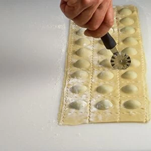 Hand using cutting wheel on sheet of ravioli, close-up