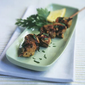 Persian lemon and saffron chicken kebab (Joojeh kabab), garnished with parsley and slice of lemon on oblong green plate
