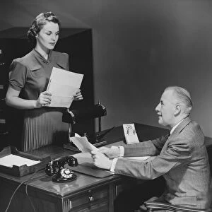 Businessman sitting at desk talking to secretary (B&W)