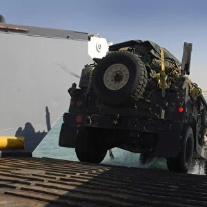 A Humvee drives down the ramp of a landing craft utility