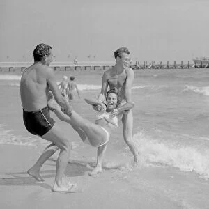 Two men throwing a young woman into the sea on Bournemouth beach. 10th Aust 1952