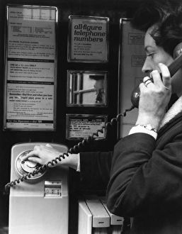 Woman dialling 999 in a public telephone box, London